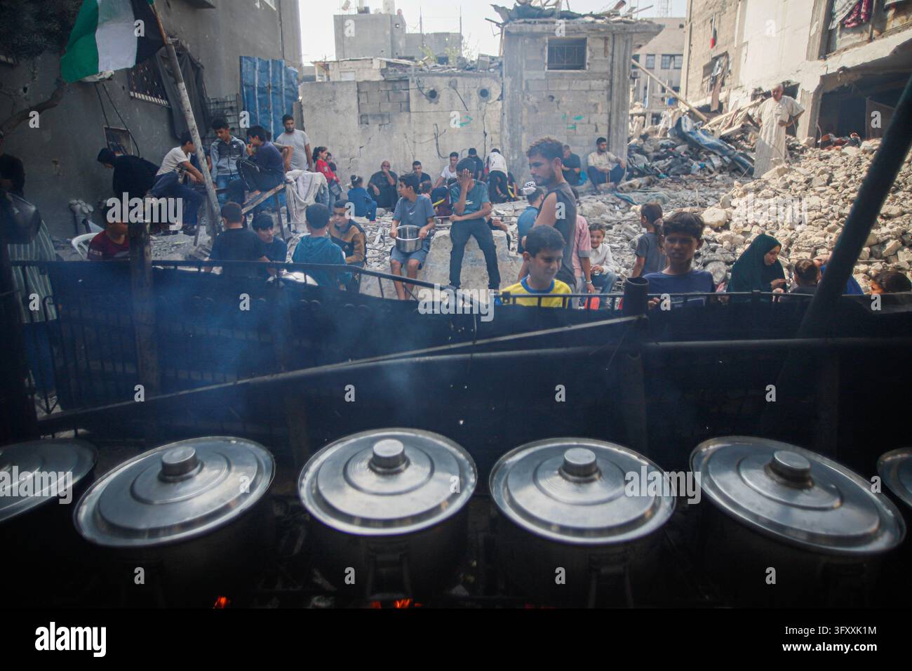 Palestinians wait behind large cooking pots as food is prepared over an ...