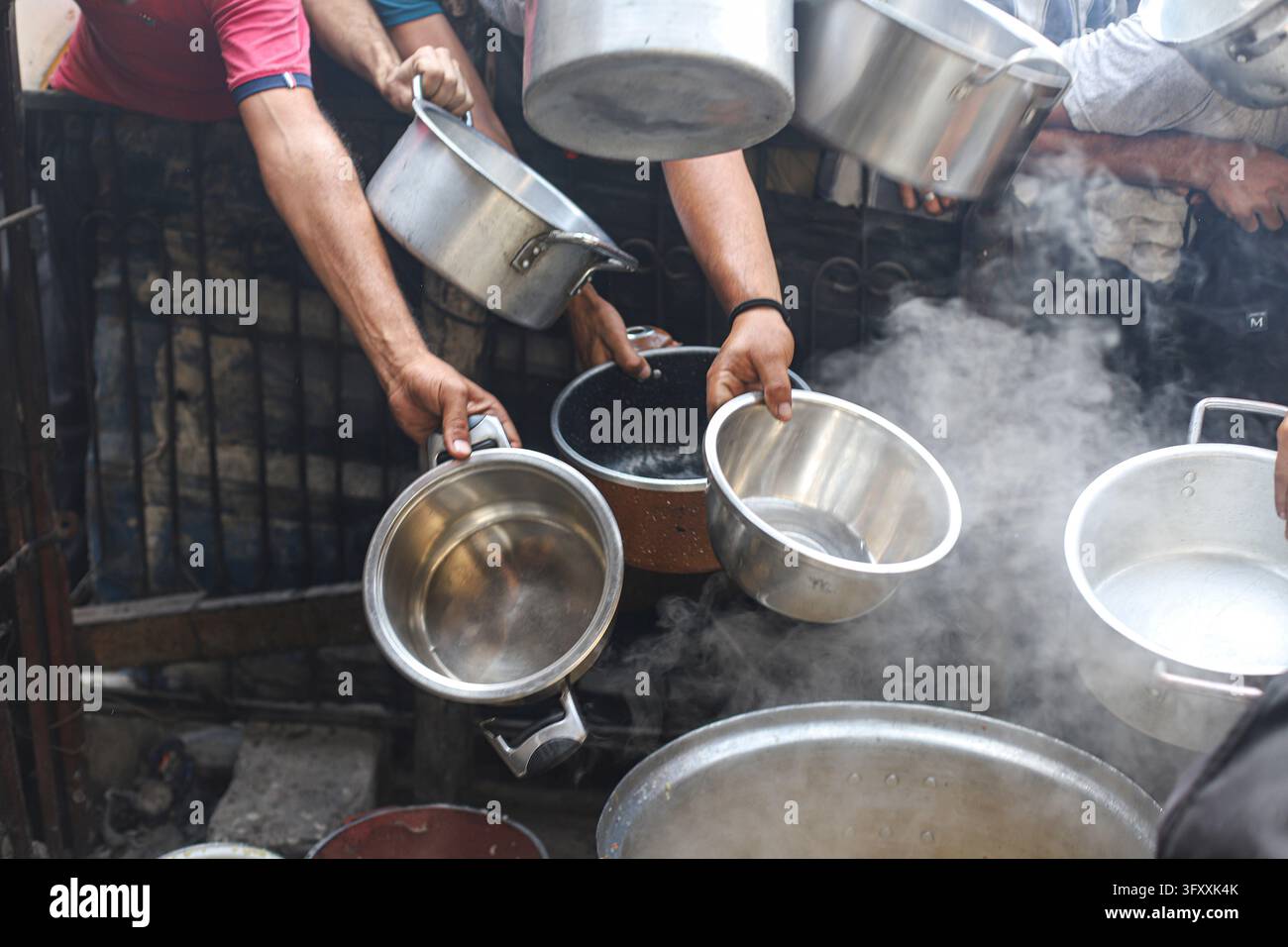 Hands hold several metal bowls over steaming cooking pots during a hot ...