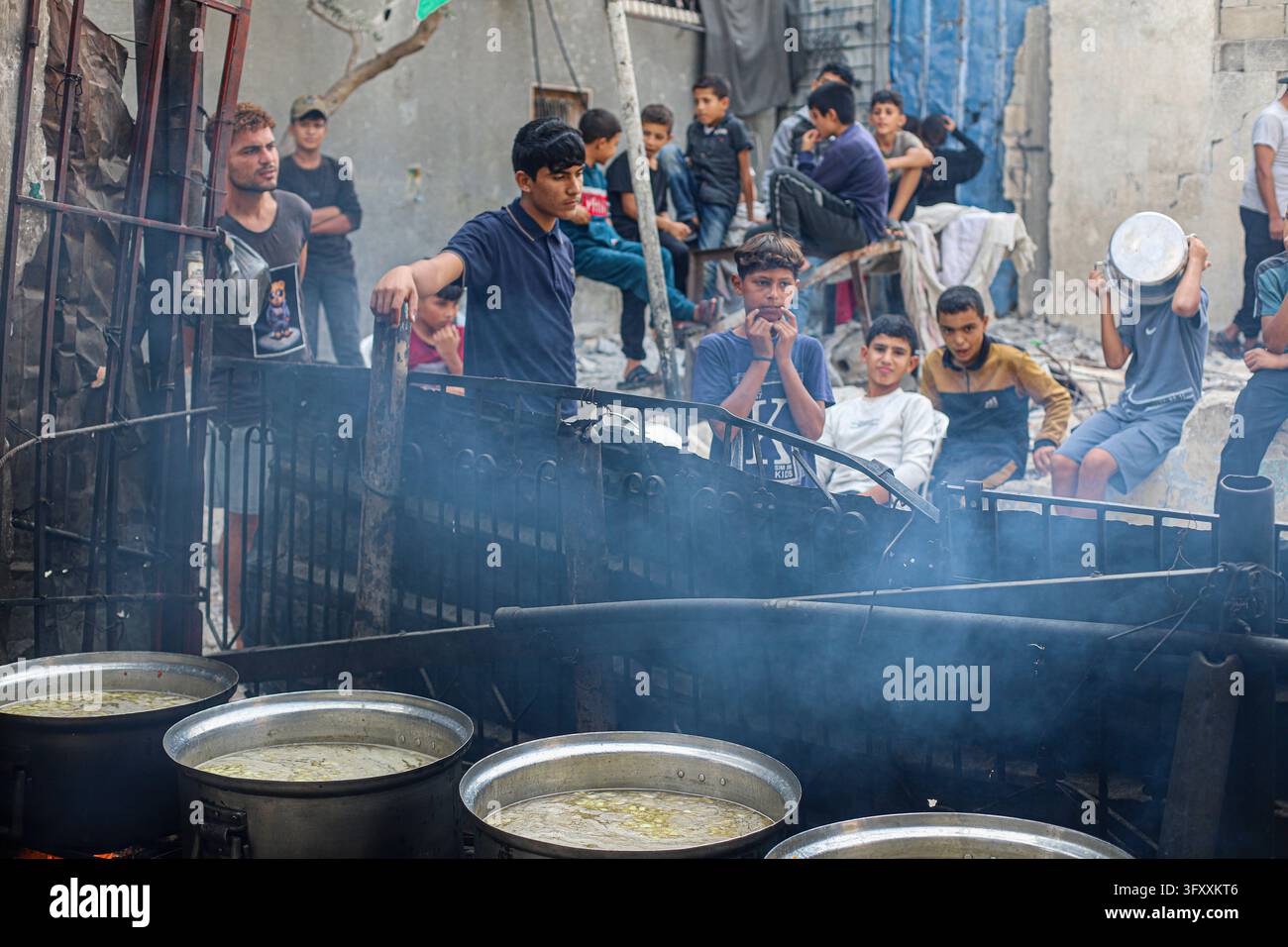 Palestinians wait behind large cooking pots as food is prepared over an ...
