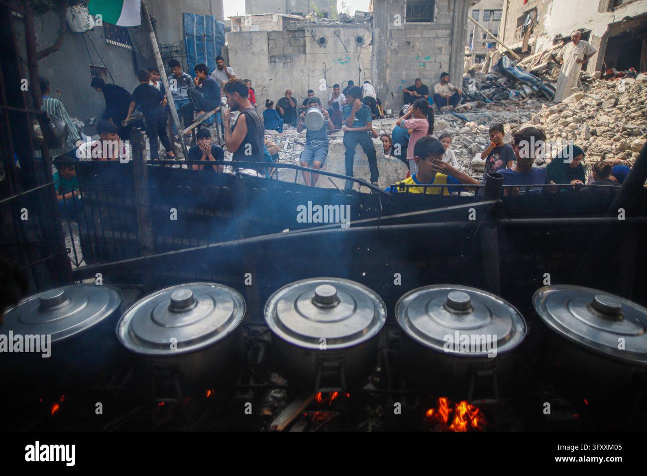 Palestinians wait behind large cooking pots as food is prepared over an ...