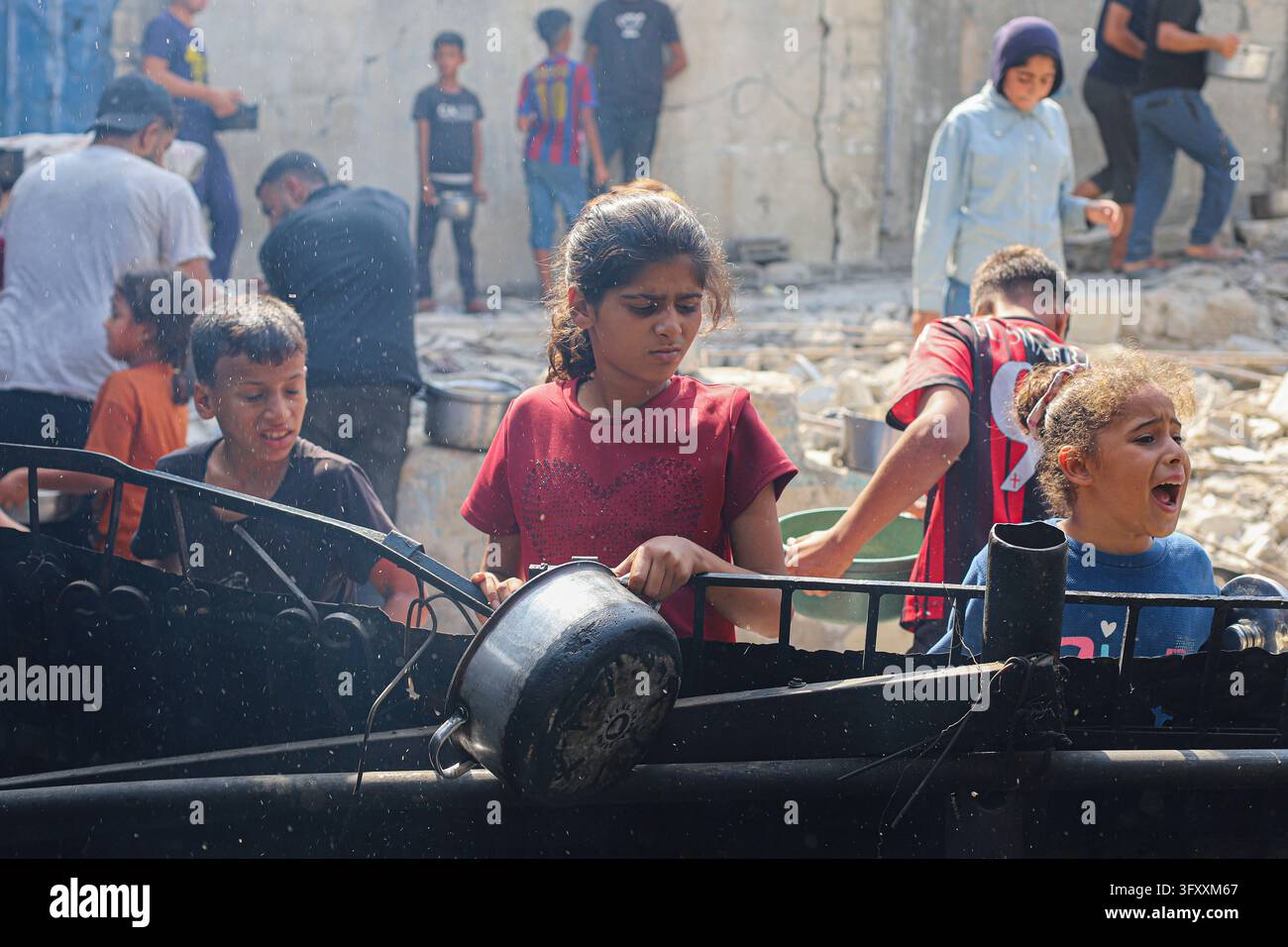Palestinian children wait with metal pots at a food distribution point ...
