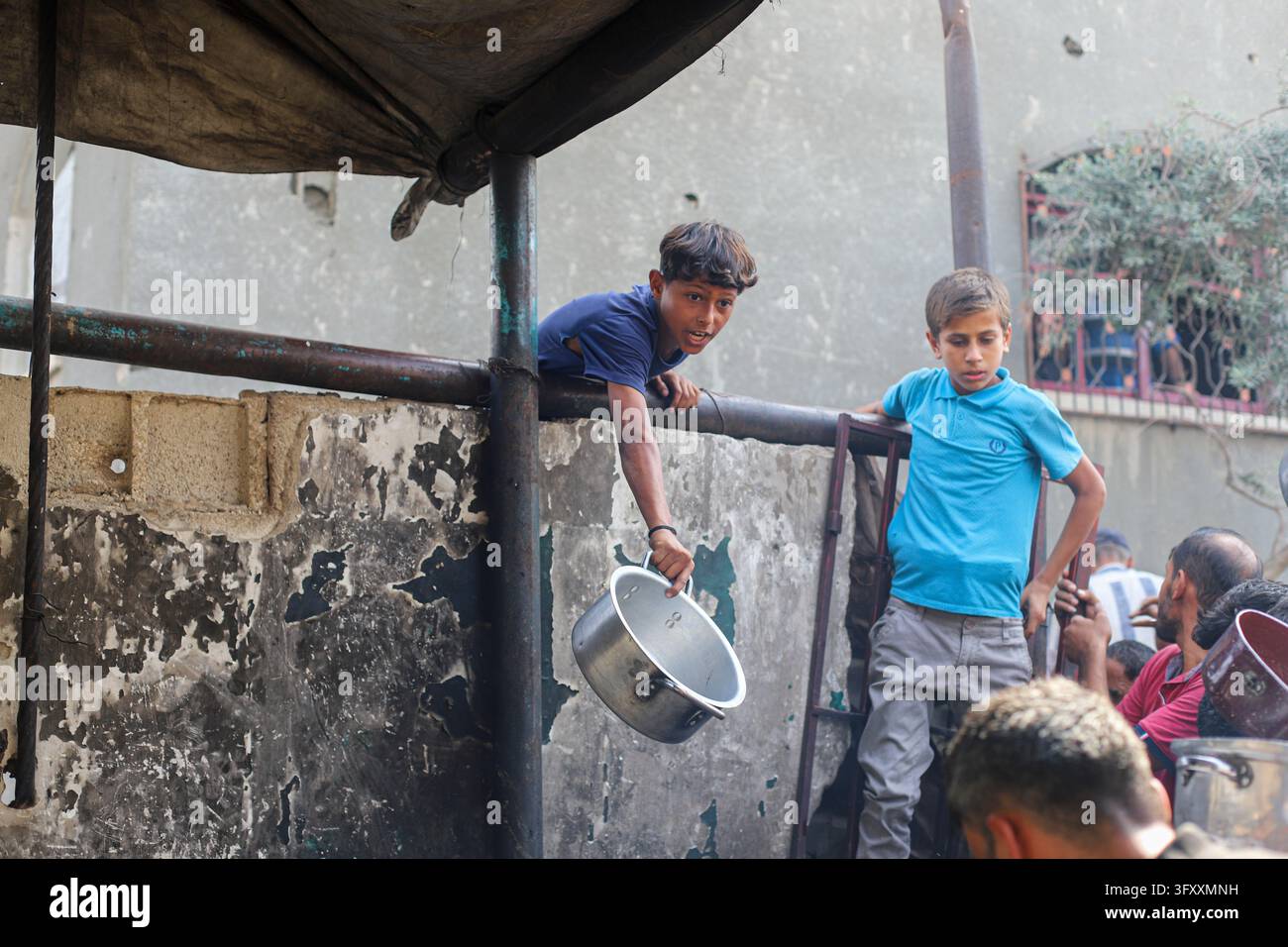 A Palestinian boy carrying a cooking pot leans over a barrier beside a ...