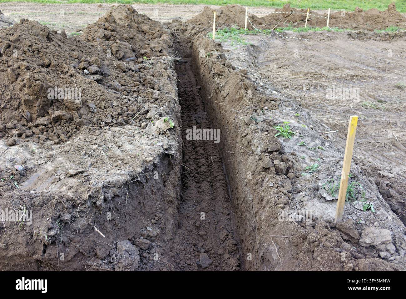 Deep narrow trench dug in brown soil for utility pipes or drainage ...