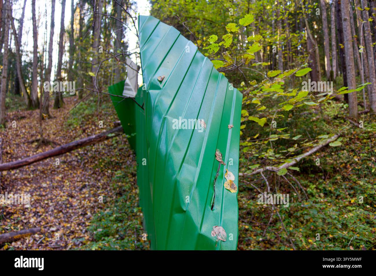 Bent green metal fence standing in a woodland area with a clear breach ...
