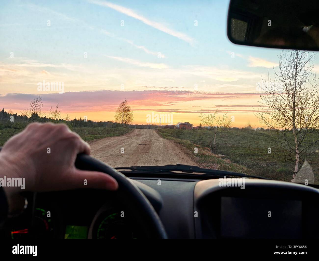 Driver view of the unpaved country road at sunset passes open fields ...