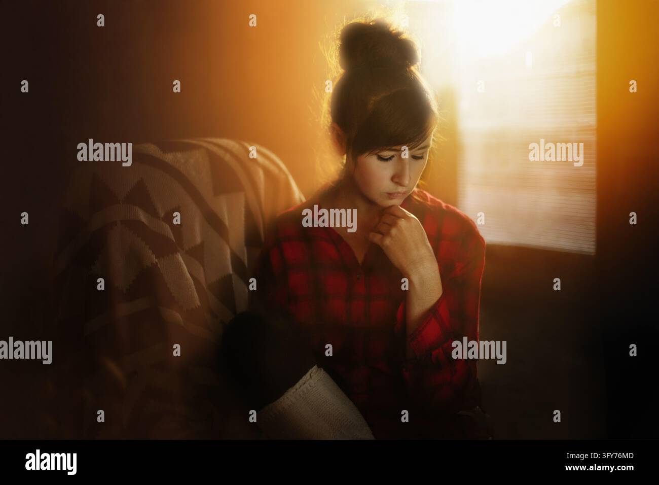 Pensive young woman sitting alone in golden sunlight Stock Photo