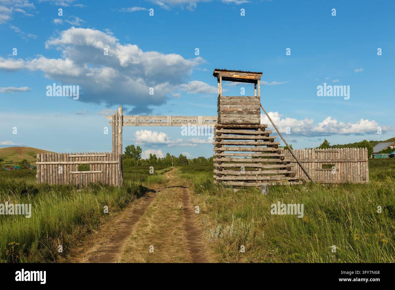Wooden watchtower and palisade gate over dirt road in green meadow ...