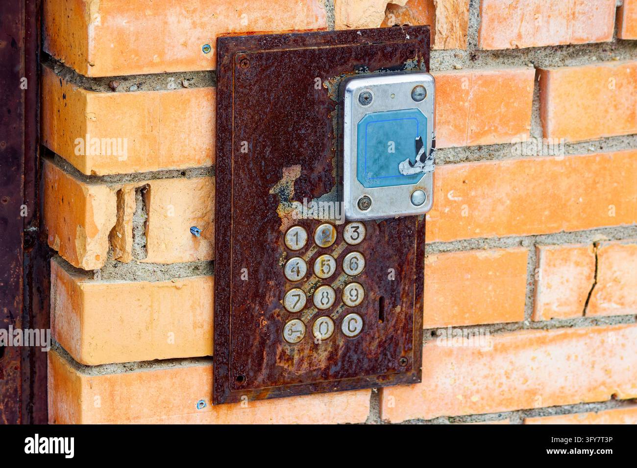 Weathered rusty intercom panel mounted on a textured orange brick wall ...