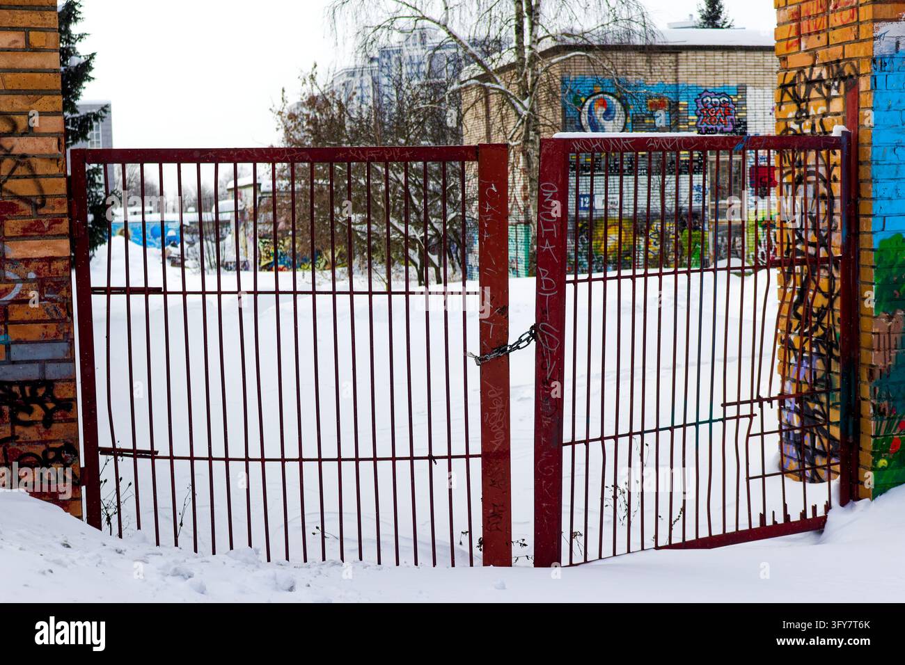 Old metal gate covered in vibrant urban graffiti blocks a snowy passage ...