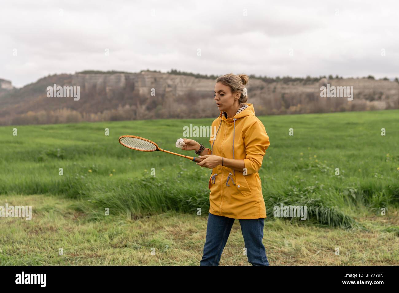 A woman in a bright yellow raincoat stands in a green grassy field ...