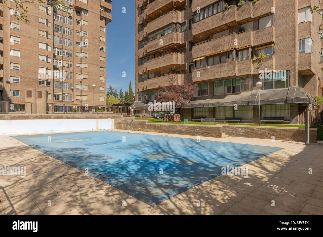 Covered community swimming pool with blue tarp surrounded by tall brick ...