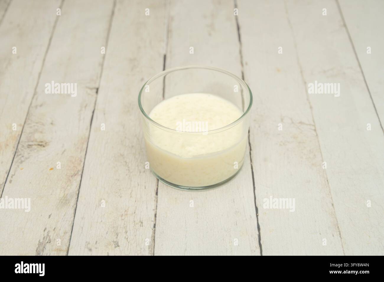 Creamy rice pudding in a small clear glass bowl on whitewashed wooden ...