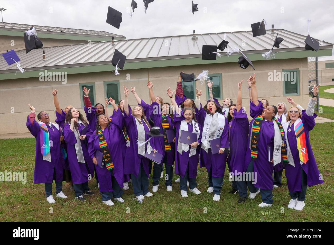 Eighteen women in purple graduation robes and mortarboards toss their ...