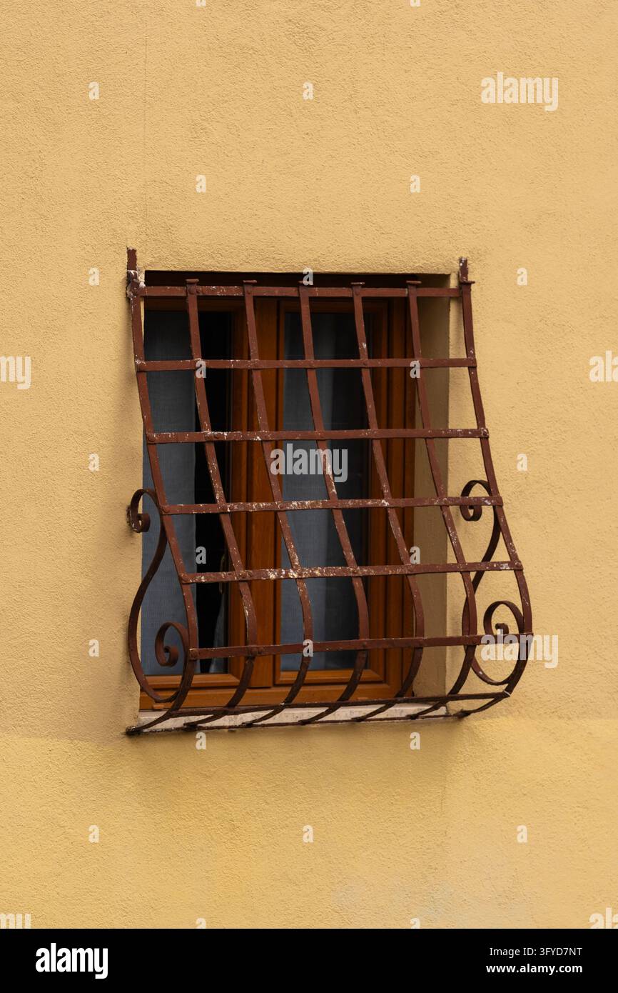 Rusty wrought iron grate on small window in yellow plastered wall Stock Photo