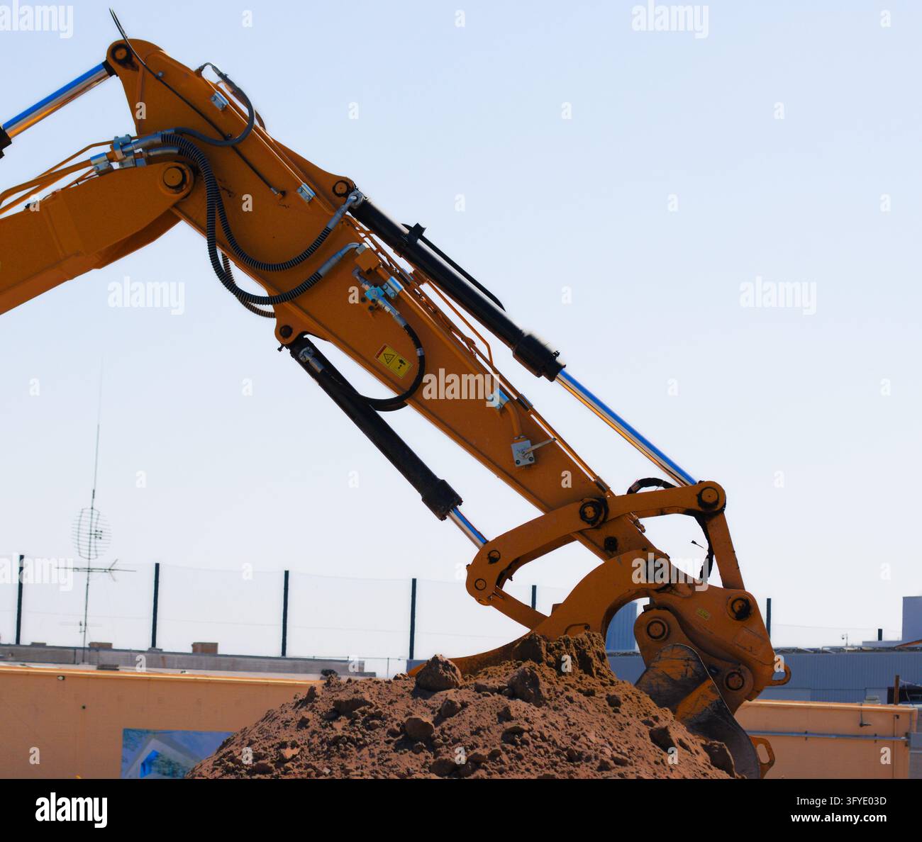 Close-up of an orange excavator arm with exposed hydraulic cylinders ...