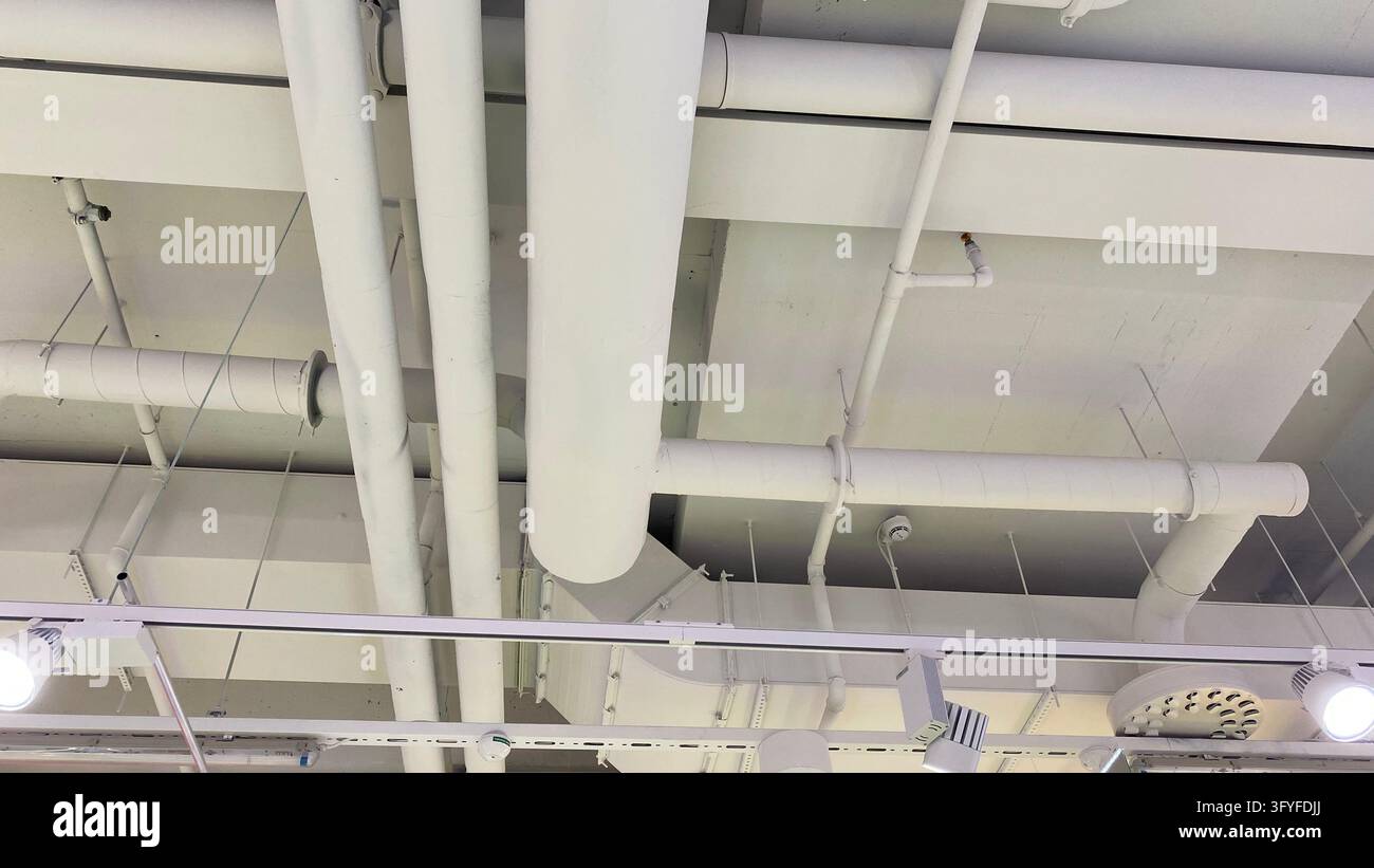 Exposed white ventilation ducts and ceiling pipes in modern industrial ...