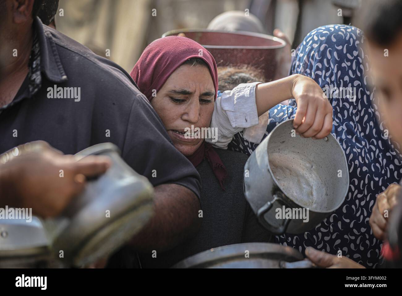 A Palestinian woman lifts a metal cooking pot above the crowd as ...