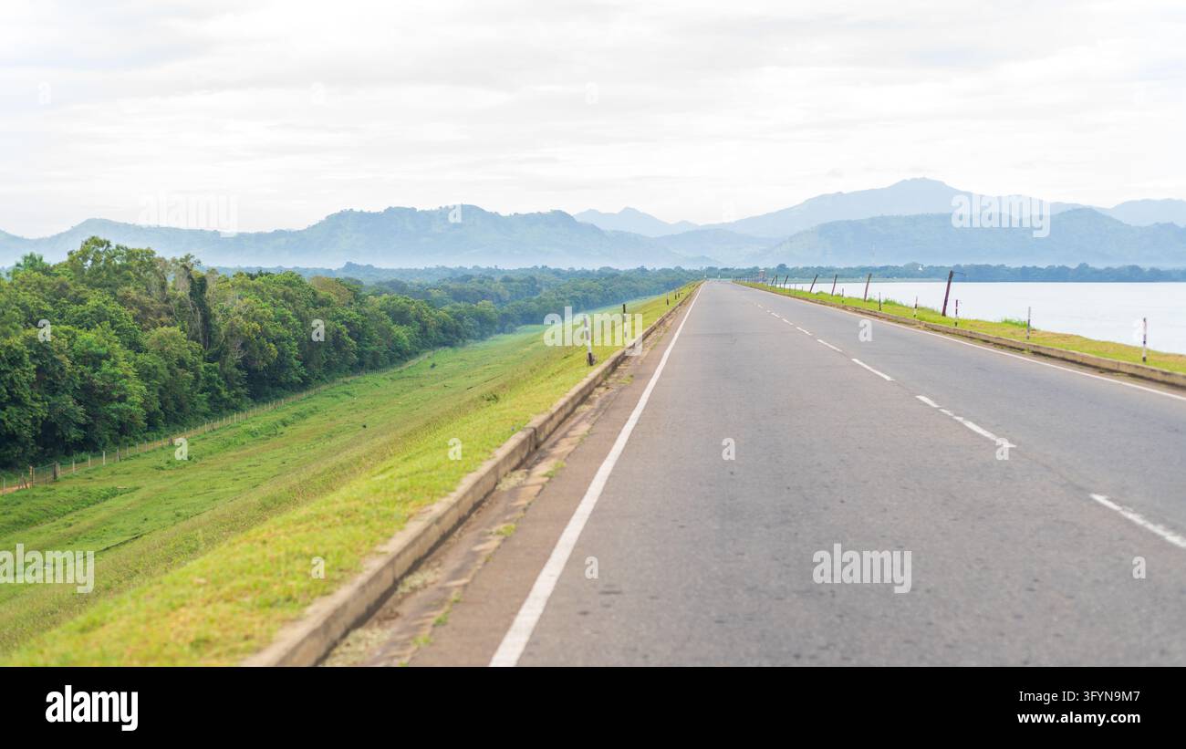 A long empty road runs along the edge of Udawalawe Reservoir, bordered ...