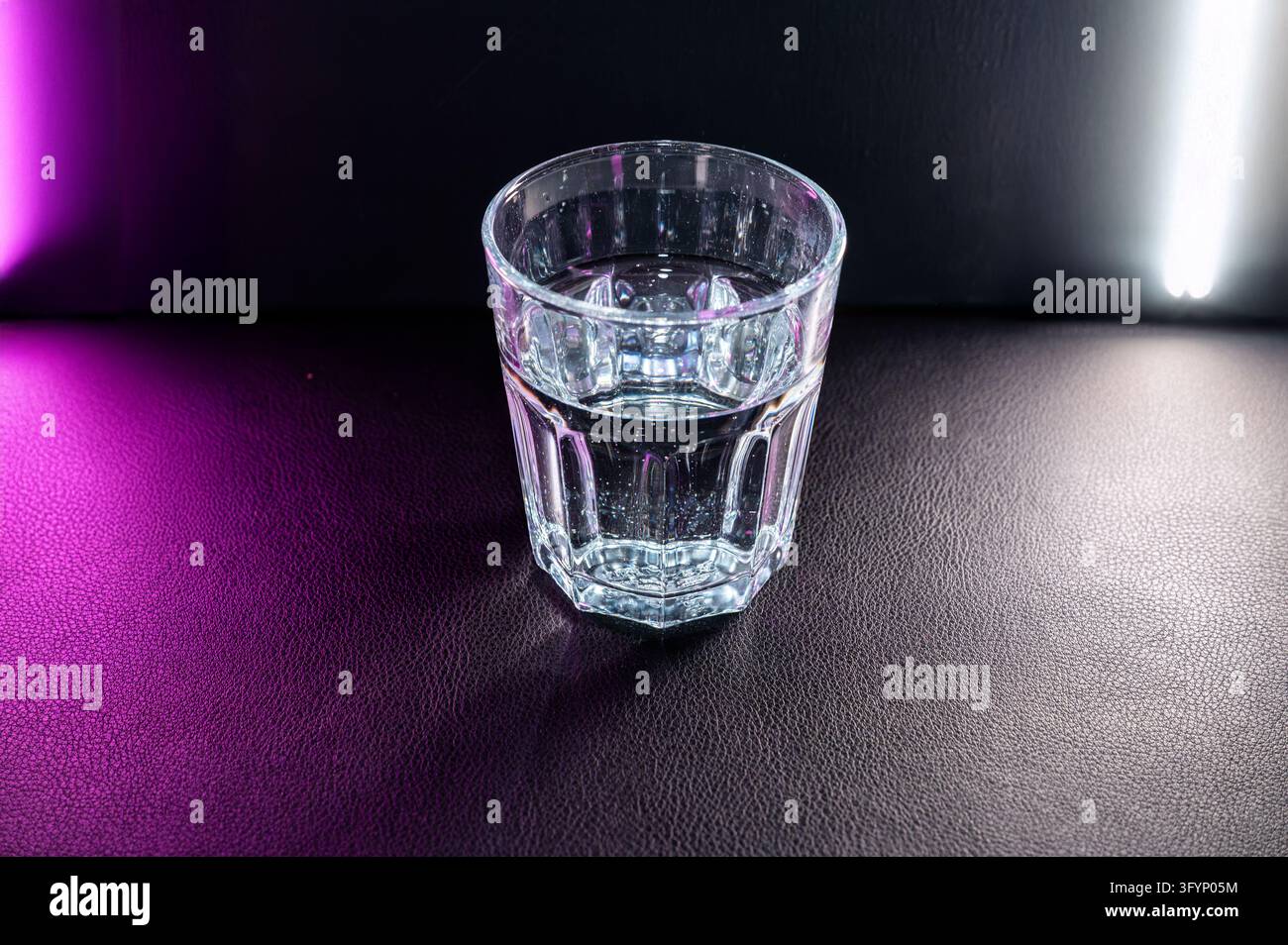 Lit Hydrations Glass of clean water stands on a dark table lit by pink side light ...