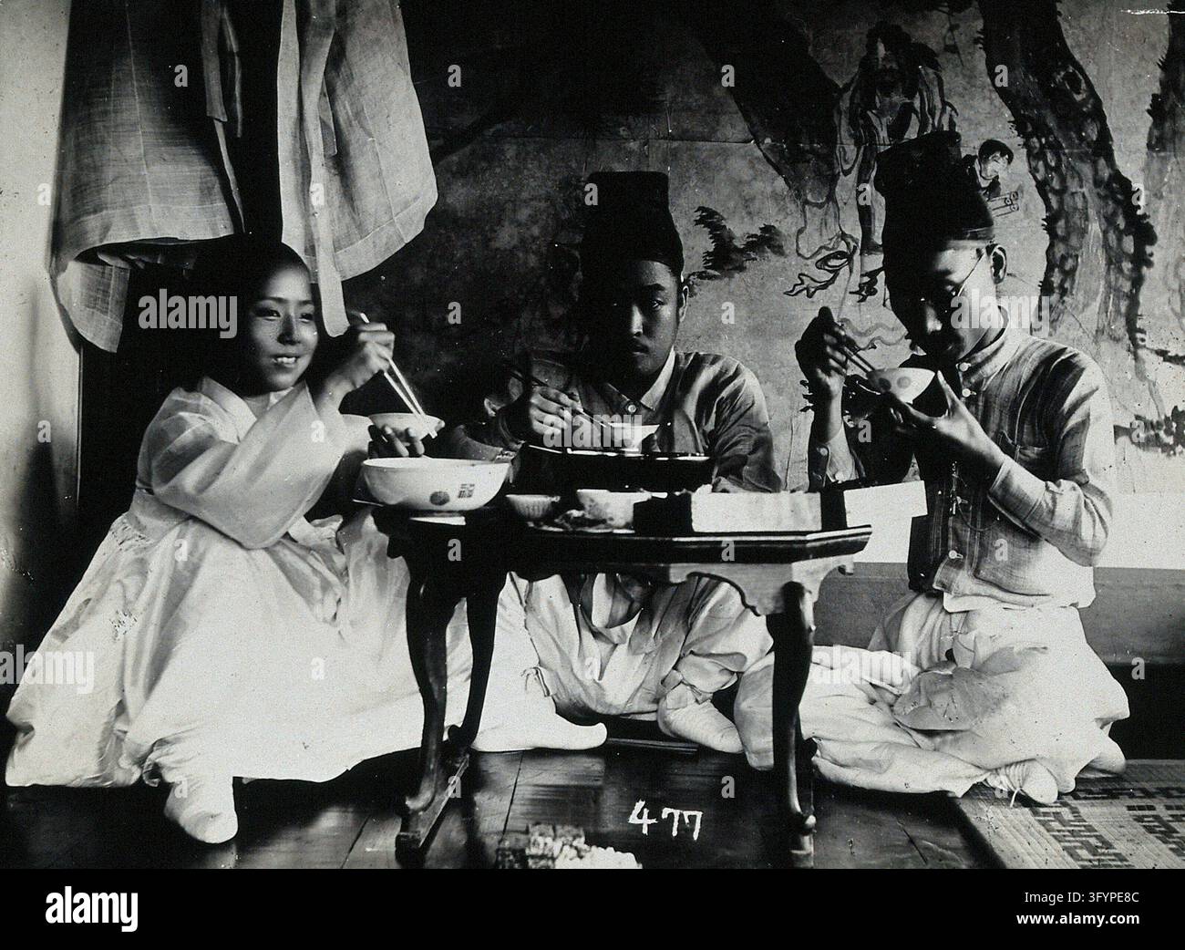 A group of people eating a meal, seated behind a small table, in front ...
