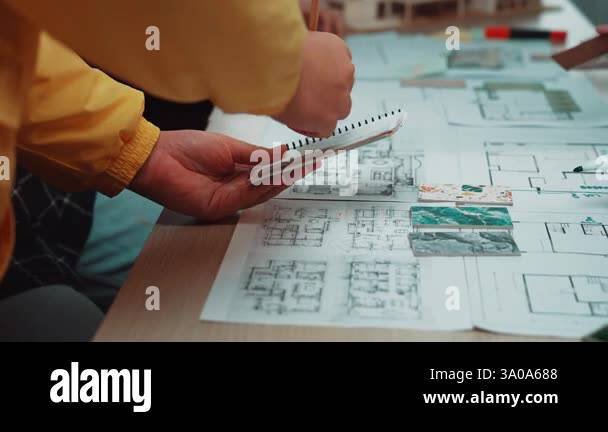 A group of designers collaborate over detailed architectural blueprints ...
