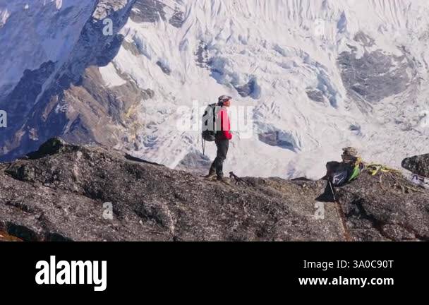 Mountain climber in red jacket atop rocky slope, gazing across majestic ...