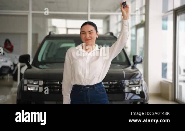 Joyful woman raising car keys in excitement while standing in front of ...