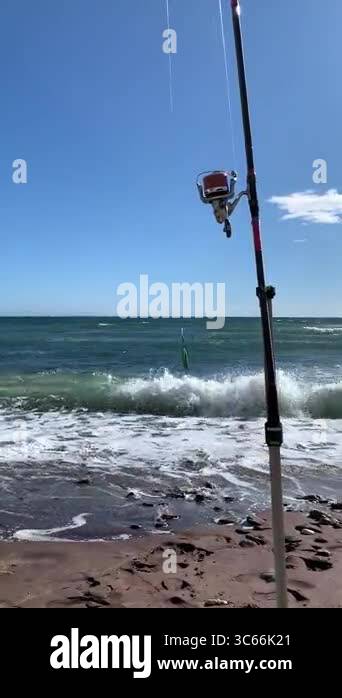 A fishing rod stands on the wet sandy shore of Costa del Sol, Andalusia ...