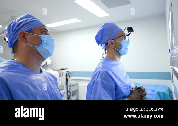 Male surgeons stand both looking at the light screen with MRI scans of ...