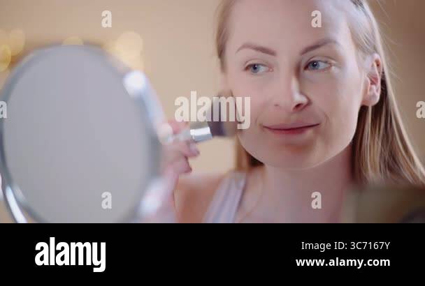 Woman using brush to apply face powder to her cheeks as part of beauty ...