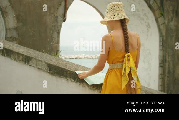 Woman views ocean from stairway - Woman Views Ocean From Stairway Under Arch Bridge In Atrani City On Amalfi Coast Italy During Summer Noon Tourist In Yellow Dress Studies A Map By The Seaside 3c71twx
