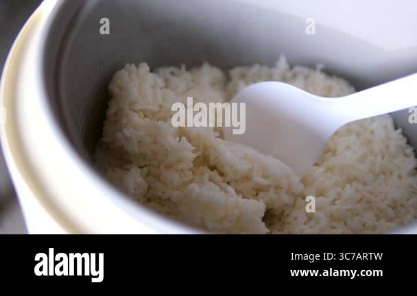 spoon stir cooked white Thai jasmine rice in a rice cooker bowl close ...