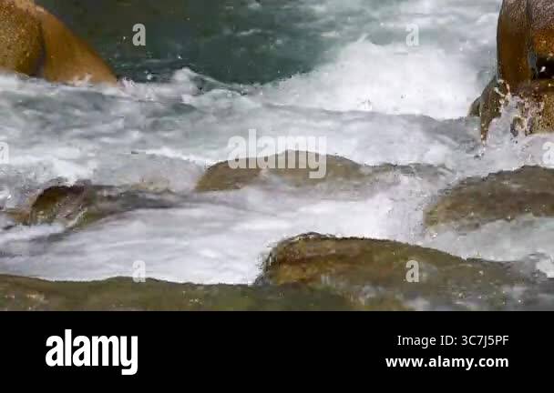 Footage of the river flowing through the stones and the white foams ...