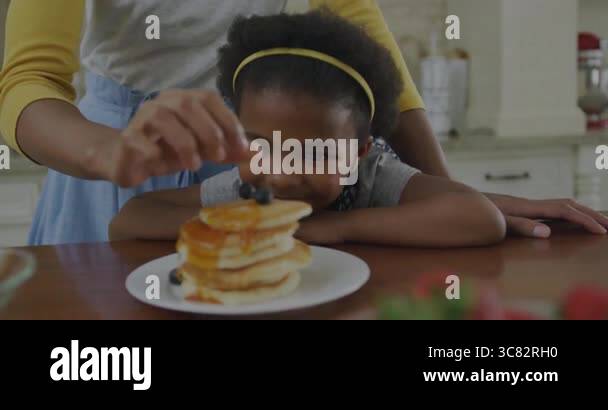 smiling-child-in-kitchen-looking-at-stack-of-pancakes-with-syrup-and