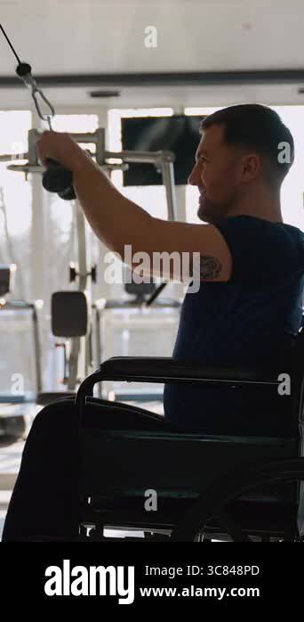 Upper Body Training Routine On Cable Machine Smiling man in a wheelchair trains upper body on a cable machine at the ...