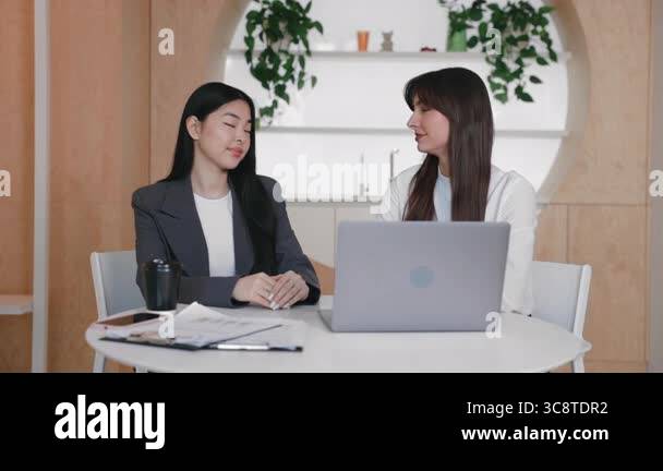 Two confident businesswomen sitting side by side with open laptop and ...