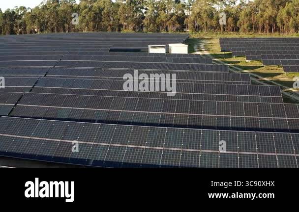 Pan left shot of a solar farm with rows of solar panels, surrounded by ...