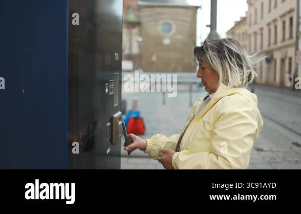 Elderly woman purchasing a tram ticket at a vending machine on a city ...
