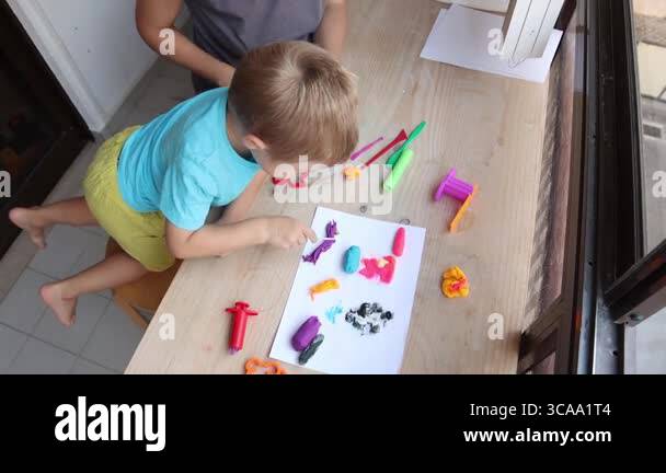 Mother and son creating colorful play dough shapes on a table Stock ...