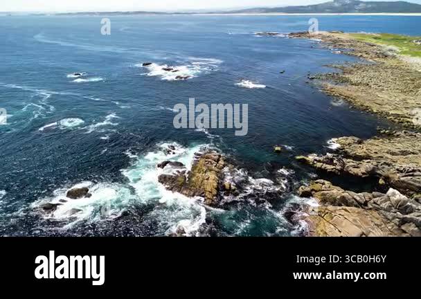 An aerial view shows a rocky coastline with waves crashing beneath blue ...