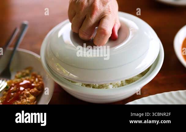 Opened Rice A hand opens a bowl of rice on a wooden table, revealing freshly cooked ...