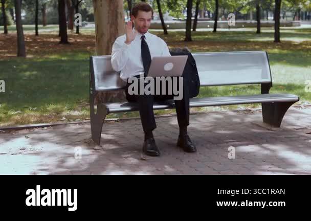 Remote work. Businessman sitting on a bench with a laptop on his lap ...