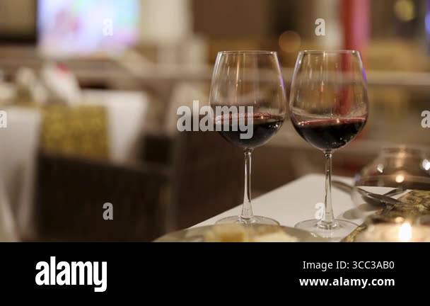 Two wine glasses on a table in a dimly lit restaurant, creating a warm ...