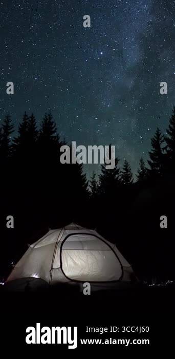 Illuminated tent under starry sky in forest at night, surrounded by ...
