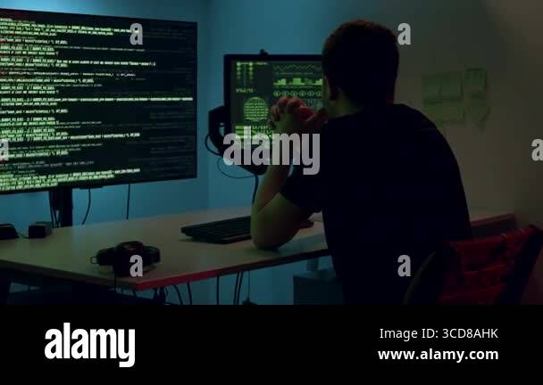 Male software developer is analyzing code on dual monitors in a dark ...