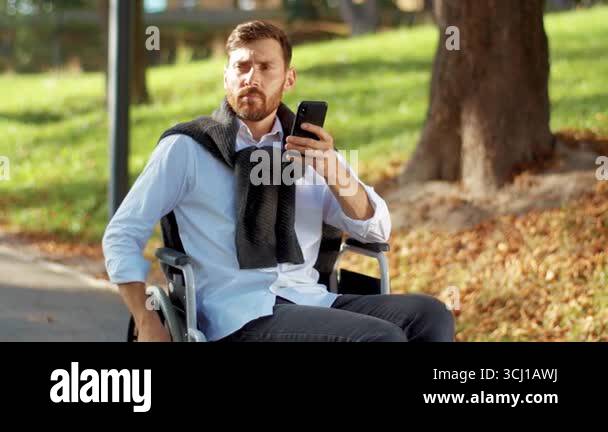 Portrait young disabled man use phone on a wheelchair in a park at ...