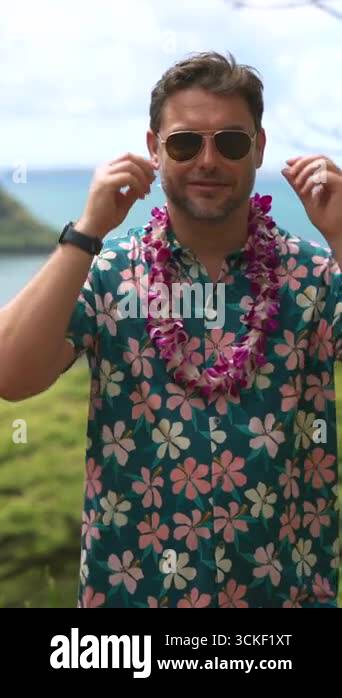Smiling man wearing a Hawaiian shirt and purple flower lei stands ...