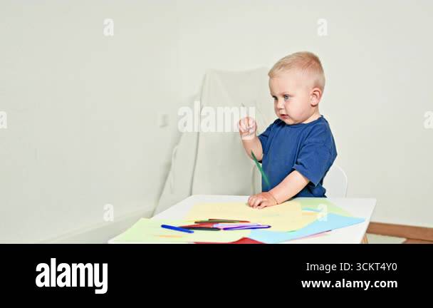 Cute 2 year old boy draws with colored pencils sitting at a children's ...