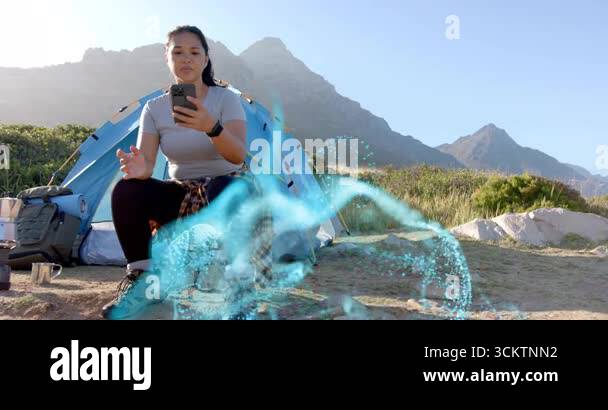 Woman in campsite tapping smartphone demonstrating AR tech glowing blue ...
