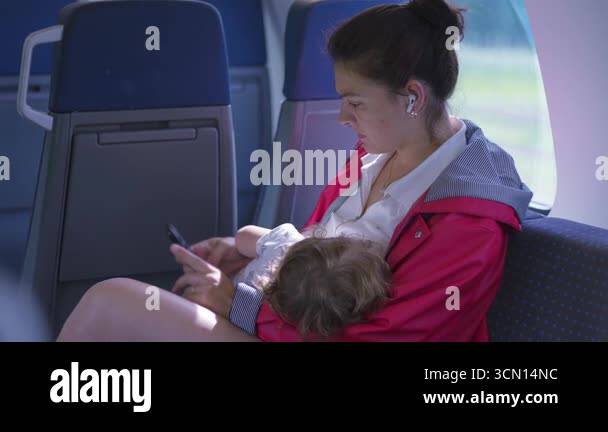 Mother Breastfeeding Child While Using Smartphone On Train Quiet mother-breastfeeding-child-while-using-smartphone-on-train-quiet